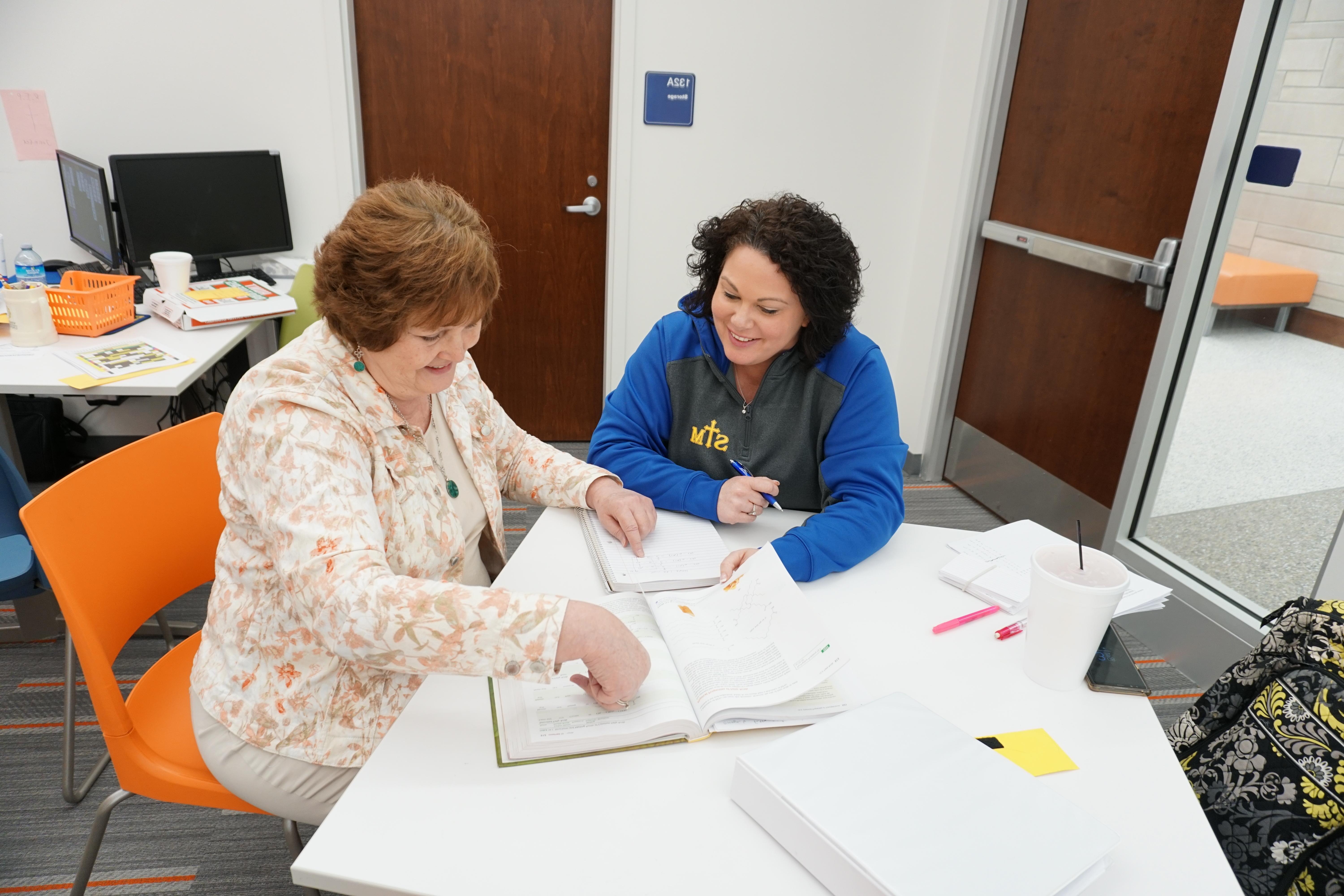 Two women looking through a textbook inside Updike Hall