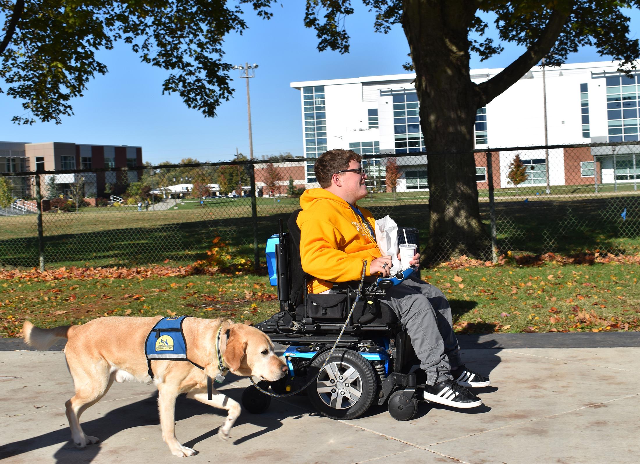 一个学生和他的服务犬在厄普代克大厅前散步